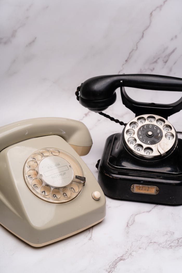 About A pair of vintage rotary phones on a marble surface, showcasing classic design.